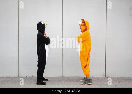 Due donne in penguin e lion costume opposta in piedi nella parte anteriore della parete di cemento Foto Stock