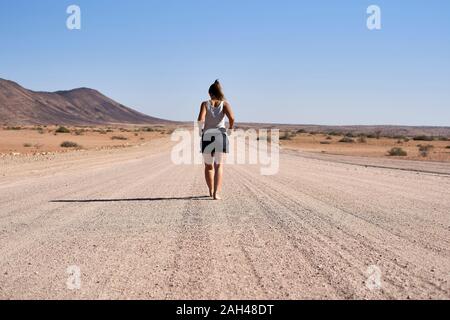 Donna che cammina nel mezzo di una strada sterrata, Damaraland, Namibia Foto Stock