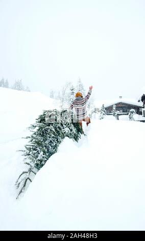 L'uomo arriva a casa, agitando e tirando verso l'albero di Natale nella neve Foto Stock