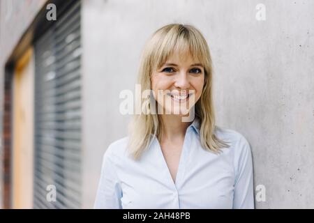 Ritratto di un sorridente giovane imprenditrice appoggiato contro una parete Foto Stock
