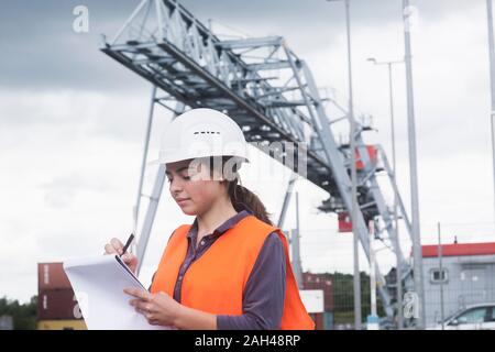 Lavoratore di sesso femminile con appunti prendere appunti sul sito industriale Foto Stock