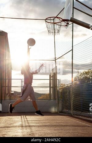 Adolescente giocare a basket, dunking contro il sole Foto Stock