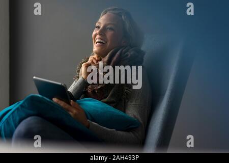 Ridendo giovane donna seduta in poltrona utilizzando tablet Foto Stock