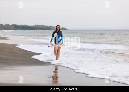 Giovane donna con la tavola da surf in spiaggia, Kedungu Beach, Bali, Indonesia Foto Stock