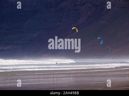 Spagna Isole Canarie Caleta de Famara, Kiteboarders a Playa de Famara con alta rupe in background Foto Stock