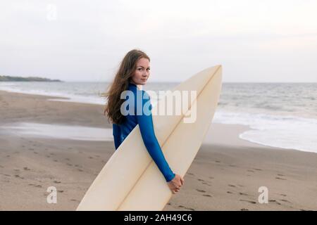 Giovane donna con la tavola da surf in spiaggia, Kedungu Beach, Bali, Indonesia Foto Stock