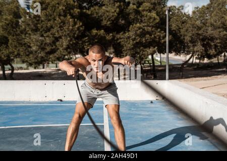 Barechested uomo muscolare esercitando con funi di battaglia all'aperto Foto Stock