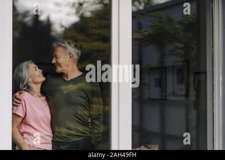 Felice coppia senior dietro il vetro di finestra di casa propria Foto Stock