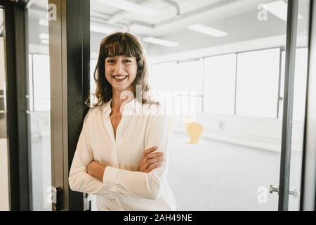 Imprenditrice sorridente in piedi in un ufficio aperto porta Foto Stock