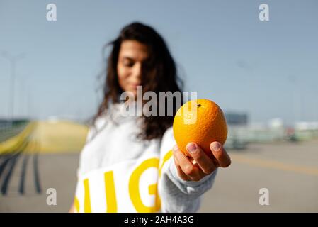 una ragazza in una felpa con cappuccio sportiva lancia un arancio come un baseball. sport, fitness Foto Stock