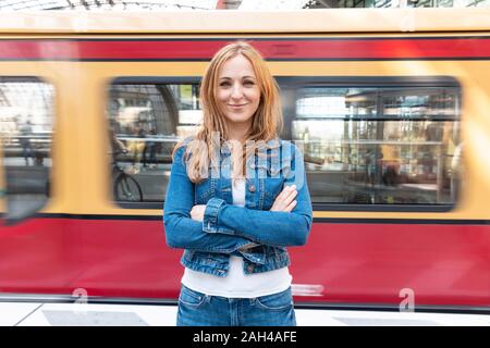 Ritratto di donna sorridente con treno sfocata in background in stazione, Berlino, Germania Foto Stock