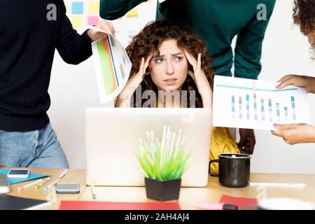 Ha sottolineato la donna posa alla scrivania in ufficio circondato da colleghi Foto Stock