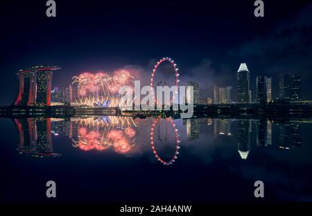 Singapore, notte di fuochi d'artificio tra Marina Bay Sands Hotel e illuminato ruota panoramica Ferris Foto Stock