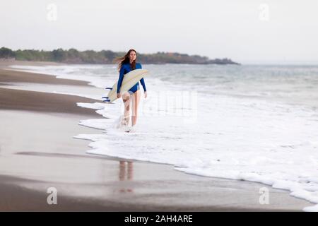 Giovane donna con la tavola da surf in spiaggia, Kedungu Beach, Bali, Indonesia Foto Stock