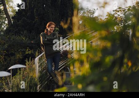 Felice donna in piedi sulle scale nel suo giardino, sorridente Foto Stock