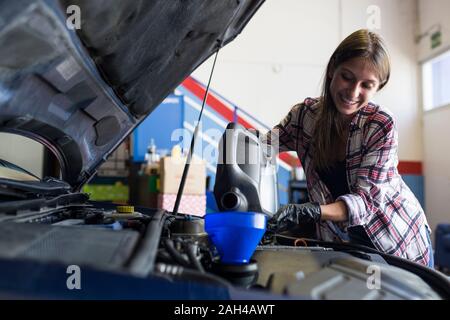 Sorridente casual donna guanti in azienda può di olio motore e di versarla attraverso imbuto in macchina lavorare in servizio Foto Stock