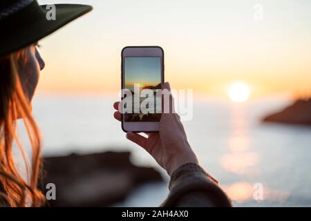 Giovane donna utilizza lo smartphone sulla spiaggia durante il tramonto, Ibiza Foto Stock