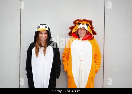 Due donne in penguin e lion costume nella parte anteriore della parete di cemento Foto Stock