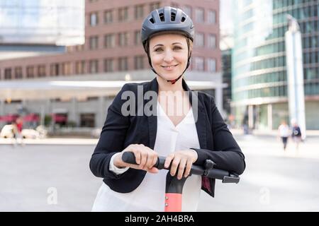 Ritratto di donna sorridente con e-scooter nella città di Berlino, Germania Foto Stock