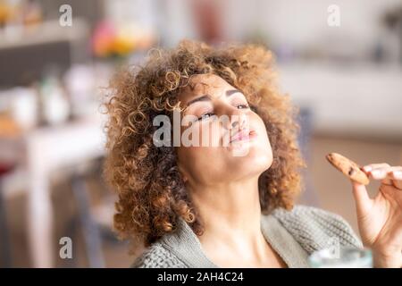 Sorridente metà donna adulta di mangiare un cookie Foto Stock