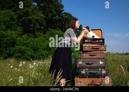 Giovane donna cuddling little dog sitter in valigia Foto Stock