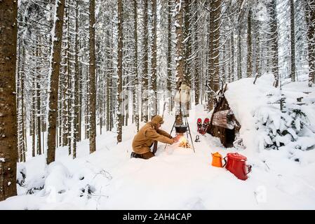 L'uomo preparando il tè in inverno foresta accanto a un rifugio in legno, Stato di Salisburgo, Austria Foto Stock