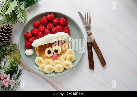 Cibo di divertimento per i bambini. Christmas Santa pancake con lampone e a banana per menu per bambini, vista dall'alto con copia spazio. Foto Stock