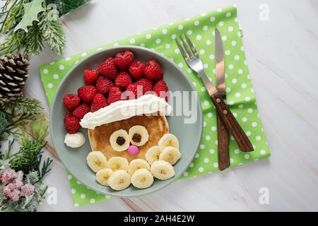 Cibo di divertimento per i bambini. Christmas Santa pancake con lampone e a banana per menu per bambini, vista dall'alto con copia spazio. Foto Stock