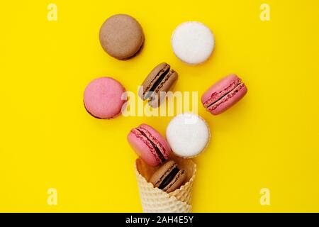 Macarons dolci. Stil life foto del cono di cialda con amaretti su sfondo giallo. Lay piatto, dessert. Foto Stock