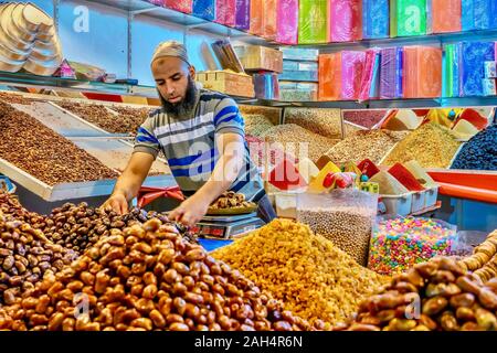 Marrakech, Marocco - 22 ottobre 2015. Un uomo marocchino in opera in un mercato pubblico di stallo che vende date, noci, spezie, caramella e confezioni regalo. Foto Stock