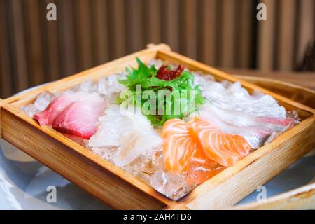 La cucina giapponese sashimi di salmone e pesce crudo sashimi insalata su ghiaccio servita sul vassoio in legno in cucina Giapponese ristorante Foto Stock