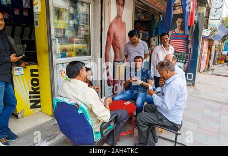 Gli uomini locali a giocare a carte sul marciapiede: scene di strada nel quartiere Mahipalpur, un sobborgo vicino all'Aeroporto di Delhi a Nuova Delhi, capitale dell'India Foto Stock