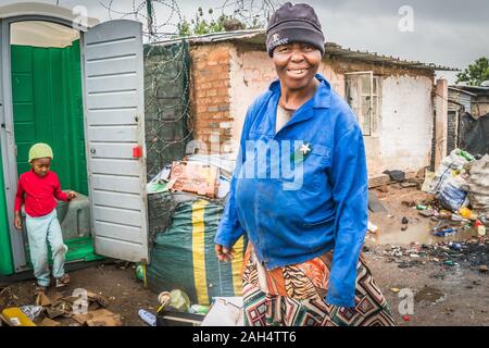 Johannesburg, Sud Africa - 4 Dicembre 2019 - Soweto baraccopoli; donna su una strada; i bambini utilizzano bagni comunali; giorno di pioggia Foto Stock