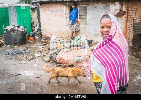 Johannesburg, Sud Africa - 4 Dicembre 2019 - Soweto baraccopoli; donne su una strada; i cani alla ricerca di cibo in cumuli di rifiuti; giorno di pioggia Foto Stock