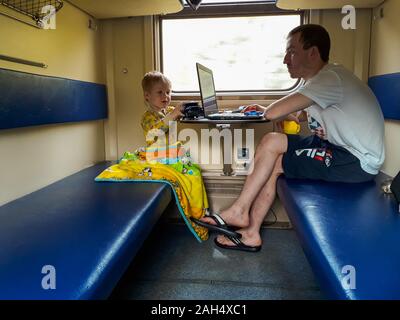 Un giovane padre e un giovane figlio andare su un treno, il Padre guarda il laptop, il bambino gioca macchine da scrivere. La ferrovia, station wagon. Viaggio. Famiglia Foto Stock