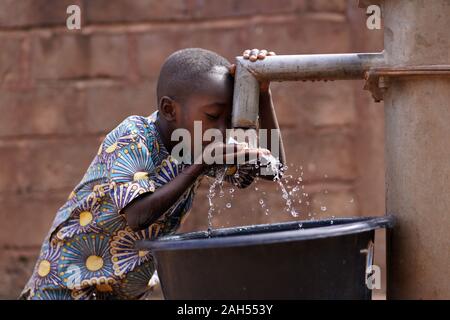 Giovane Ragazzo Africano Bere Acqua Dalla Comunità Borehole Pompa A Mano Foto Stock