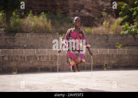 Sorridente giovane ragazza africana in fase di riscaldamento con una corda da salto in cortile Foto Stock
