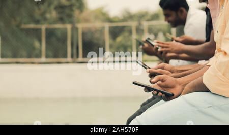 Close up di mani,giovani essendo addicted a dispositivi - gruppo di amici seduti in coda utilizzando telefoni presso la piscina - Concetto di millennial occupato Foto Stock