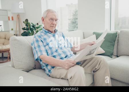 Ritratto di sua egli unico focalizzato nizza concentrata nella pace il nonno, seduto sul divano la lettura di notizie del mondo di carta alla luce interno bianco soggiorno-r Foto Stock