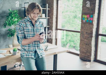 Ritratto di concentrato di persona, azienda utilizzando il dispositivo indossando occhiali eyewear a scacchi in plaid shirt in piedi in campo industriale Foto Stock