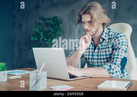Close up foto di avvocato con capelli biondi toccando il suo mento ponderando texting indossa, a scacchi plaid shirt occhiali eyewear seduta in campo industriale Foto Stock