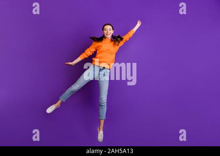 Full Size photo positiva di allegro teen ragazza attesa salto a mano la sua cattura battenti, parasol sul tempo ventoso usura arancione abbigliamento sportivo jeans sneaker bianco Foto Stock