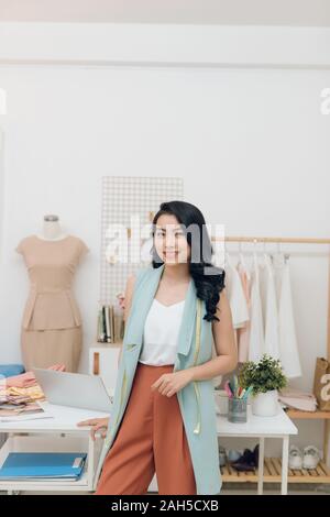 Giovani asiatici designer di moda sorridente e in piedi davanti al banco in officina Foto Stock