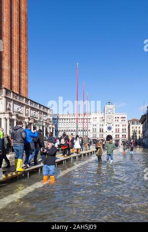 Acqua Alta inondazioni durante l estrema alta marea Piazza San Marco, Venezia, Italia con i turisti a piedi su passeroles o passerelle elevate nella parte anteriore del Foto Stock