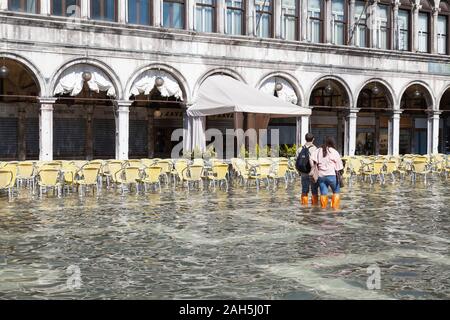 Acqua Alta inondazioni durante l estrema alta marea Piazza San Marco, Venezia, Italia. I turisti - eyeing ristorante vuoto sedie al Caffe' Laverna in acqua di inondazione Foto Stock