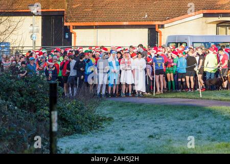 Chippenham, Wiltshire, Regno Unito. 25 dicembre, 2019. I corridori sono illustrati in quanto essi allineati sulla linea di partenza di un inizio di mattina del giorno di Natale 5km parkrun in Monkton Park, Chippenham, Wiltshire. 400-500 persone partitcipated in caso con molti vestirsi in costume. Credito: Lynchpics/Alamy Live News Foto Stock