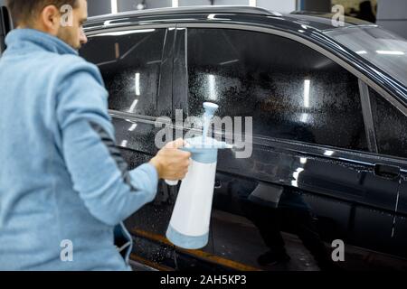 Auto di servizio lavoratore gli spruzzi di acqua sul corpo vettura, bagnando prima di anti-ghiaia film applicare al veicolo che dettaglia service Foto Stock