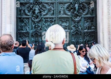 I turisti di apprezzare la bellissima bassorilievi sulla porta di bronzo della costruzione del Duomo di Milano, la chiesa cattedrale di Mila Foto Stock