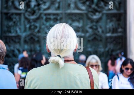 I turisti di apprezzare la bellissima bassorilievi sulla porta di bronzo della costruzione del Duomo di Milano, la chiesa cattedrale di Mila Foto Stock