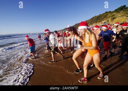 Circa 1.200 persone hanno preso parte all'annuale del giorno di Natale Macmillan Caring Bianco Natale Dip 25/12/2019. La gente in costume e su una luminosa mattina di sole corse in mare su Boscombe fronte mare. La raccolta di fondi per la cura Macmillian localmente le cure palliative unità in Christchurch, questo evento è cresciuto nel corso degli anni. Circa un quarto di milione di è stata sollevata poiché gli eventi inizi. Foto Stock